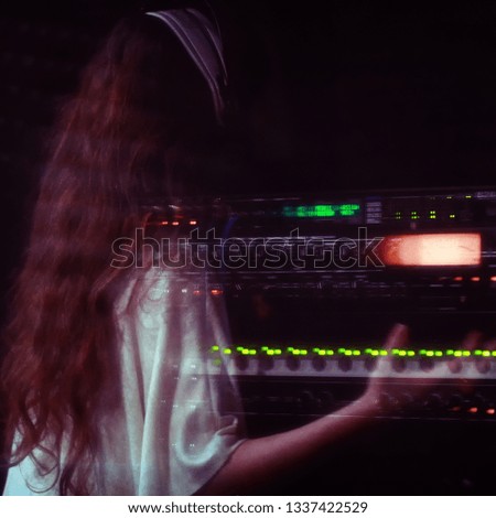 A girl in a white dress with long hair sings behind a microphone. Professional singer performs vocals in the recording Studio. Reflection in the glass of a woman who sings (square for instagram)