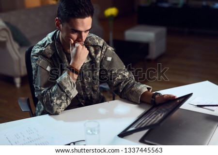 Young army soldier feeling homesick while looking at American flag in picture frame. 