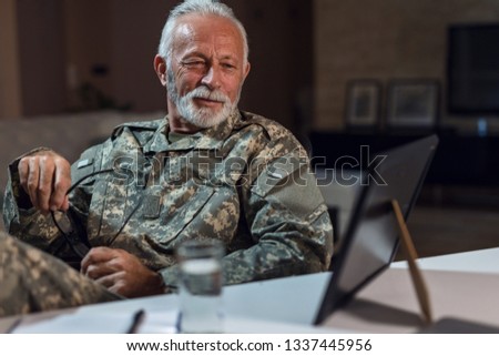 Smiling soldier in military uniform looking at framed photo on his desk and feeling nostalgic. 