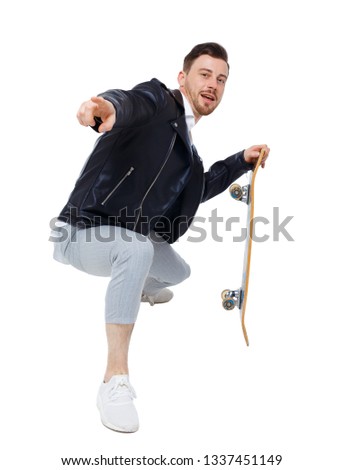A man with a skateboard. A guy in stylish clothes and trousers posing with a board for skating. Front view. Collection of sports people. Skater in skater pants shows his hand in the frame.