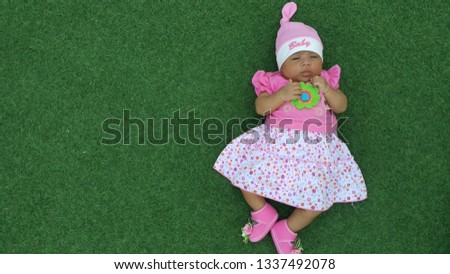 Cute baby wearing a pink dress and pink headgear against a natural green background.