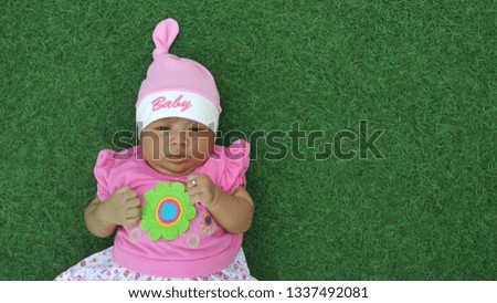 Cute baby wearing a pink dress and pink headgear against a natural green background.