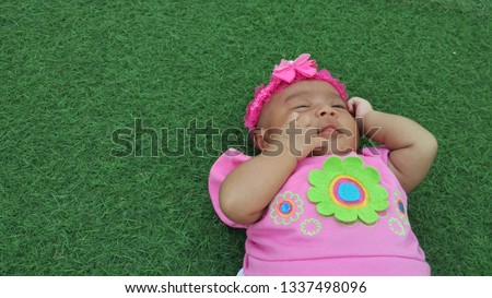 Cute babies wear pink dresses and bandana with pink floral motifs with natural green backgrounds.