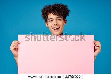 Handsome curly guy holds in front of him a pink mockup Poster blue background