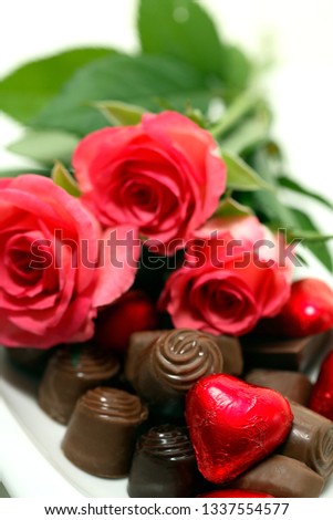 close-up of pink roses, chocolate pralines and a red heart-shaped one
