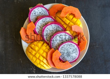 Tropical fruits assortment on a white plate, closeup. Many colorful ripe tropical fruits background. Mango, papaya and pitahaya or dragon fruit 