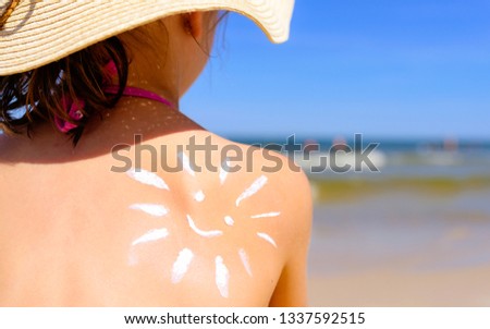 Girl with suntan lotion at the beach in form of the sun in a straw hat