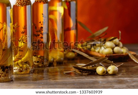 Green olives and bottles of olive oil with spices and herbs on a old wooden table.