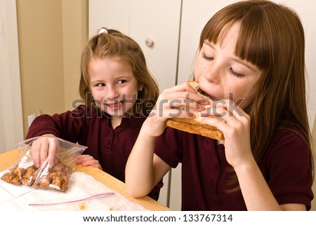 Young school girl eating lunch while a younger girls sneaks a pretzel