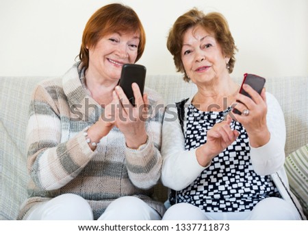Happy glad positive mature women browsing internet on smarthphones indoor Royalty-Free Stock Photo #1337711873