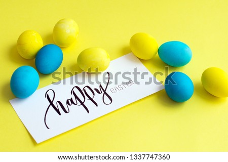Multi-colored Easter eggs, yellow, white, blue eggs on a yellow background with a greeting card "Happy Easter"