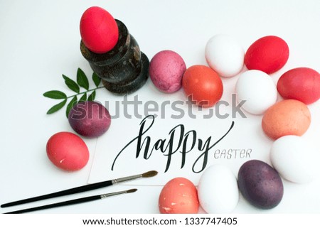 multicolored easter eggs, red, purple, pink, burgundy, lilac, white flowers on a white background with a greeting calligraphic card with the inscription "happy ester"