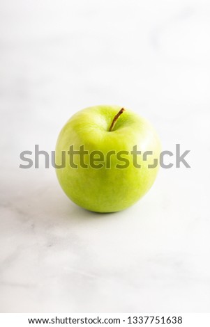 Green granny smith apple on a white marble surface