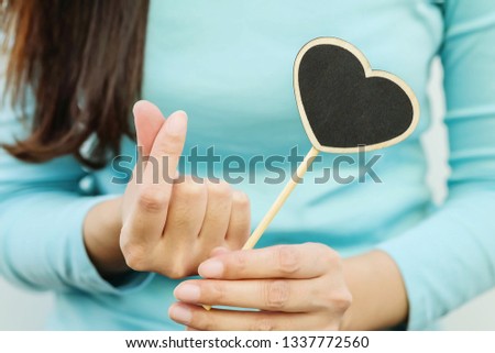 Closeup wooden black board in heart shape with finger of woman in mini heart symbol