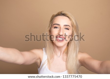 Image of excited happy young woman isolated over beige background make selfie by camera. 