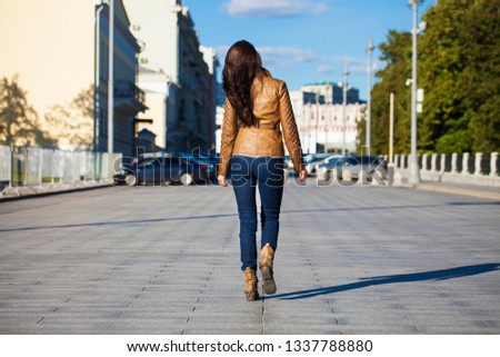 Street fashion image of young brunette woman in blue jeans and brown leather jacket