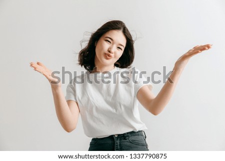 Happy asian woman standing and presenting something isolated on gray studio background. Beautiful female half-length portrait. Young emotional woman. The human emotions, facial expression concept.