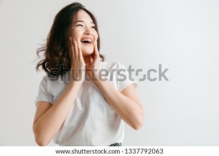 Happy asian woman standing and smiling isolated on gray studio background. Beautiful female half-length portrait. Young emotional woman. The human emotions, facial expression concept.