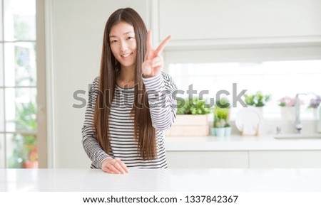 Beautiful Asian woman wearing stripes sweater smiling looking to the camera showing fingers doing victory sign. Number two.