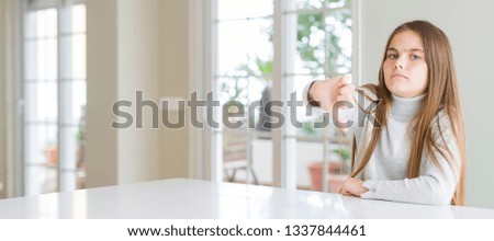 Wide angle picture of beautiful young girl kid wearing casual sweater looking unhappy and angry showing rejection and negative with thumbs down gesture. Bad expression.