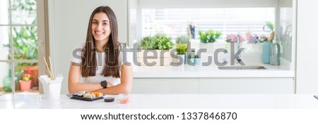 Wide angle picture of beautiful young woman eating asian sushi from delivery with a happy and cool smile on face. Lucky person.
