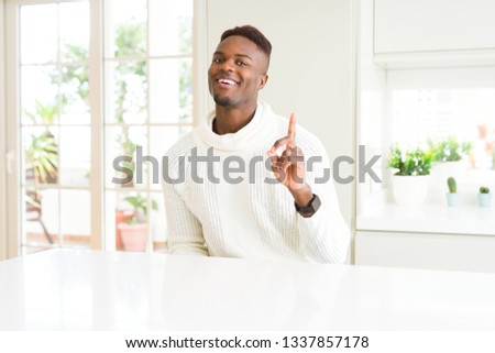 Handsome african american man on white table pointing finger up with successful idea. Exited and happy. Number one.