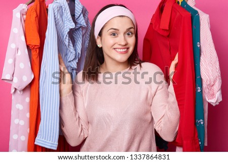 Happy smiling girl stands between hangers with blouses in fashion store. Cheerful woman visits boutique. Cute lady likes to go to mall. Beautiful young female on sale. Shopping and fasion concept. Royalty-Free Stock Photo #1337864831