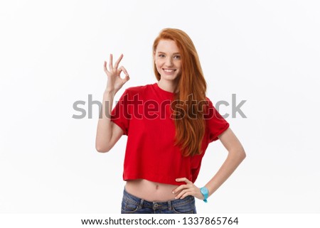 Portrait of a pretty woman in red santa claus dress showing okay sign and winking over white background.