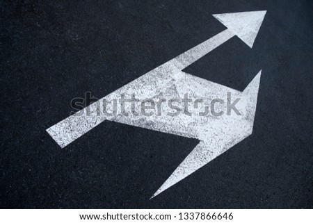 Perspective view of near black asphalt road surface showing a direction split arrow in white paint, high contrast and selective focus.