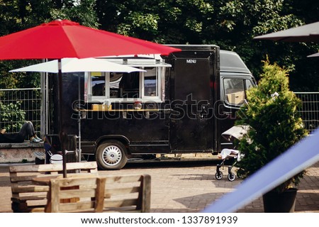 Food van truck. Stylish black mobile food truck with burgers and asian food at street food festival. Summer eating market in the city. Space for text, menu Royalty-Free Stock Photo #1337891939