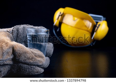 A shot of vodka and a bottle on a workshop table. Workwear and alcohol in the workshop of construction workers. Dark background.