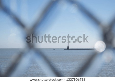 A distant light tower framed by an ice covered gate.