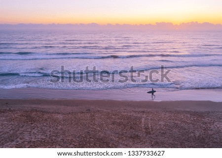 Surfer silhouette walking on ocean beach at dawn with copy space