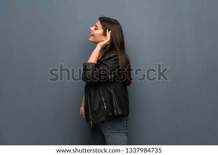 Teenager girl over grey wall listening to something by putting hand on the ear