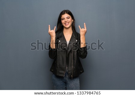 Teenager girl over grey wall making rock gesture