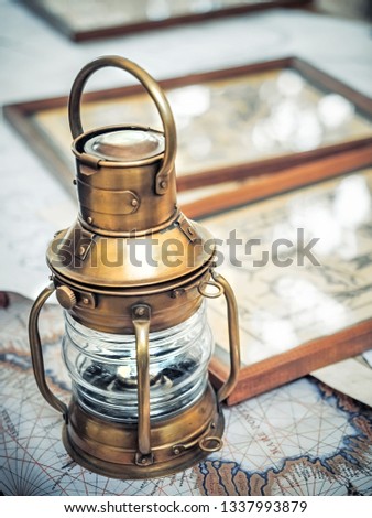 Old brassy ship lantern stands on a map of the seas near pictures with the image of sea knots