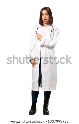A full-length shot of a Young doctor woman surprised and pointing side over isolated white background