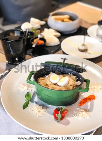 fettuccine pasta with rabbit and egg in a metal dish on a served restaurant table (parmesan, tomato)