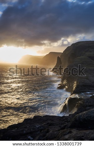 Vertical picture of colorful sunset over the wild rocky coastline and storm atlantic ocean in Faroe island Vagar during spring evening. Faroe islands, wild scandinavian landscape of rocks and cliffs.
