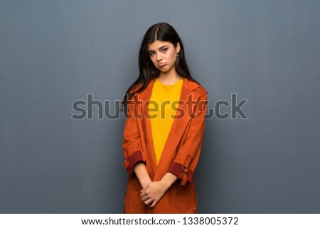 Teenager girl with coat over grey wall with sad and depressed expression