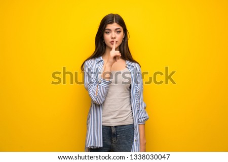 Teenager girl over yellow wall showing a sign of silence gesture putting finger in mouth