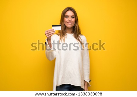 Blonde woman over yellow wall holding a credit card