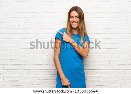 Woman with blue dress over brick wall pointing to the side to present a product
