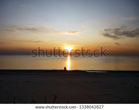 Against the background of the sunset, a couple is walking along the seashore