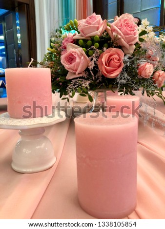Pink candles on pink tablecloth with pink roses wedding bouquet on the table