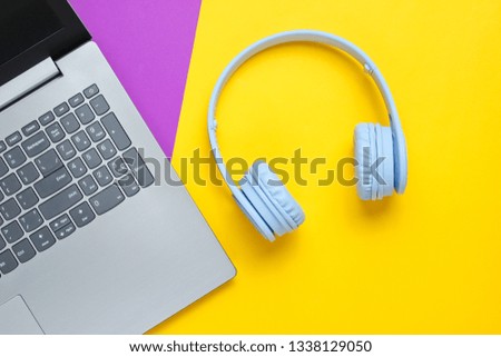 Modern gadgets. Laptop, wireless headphones on a purple-yellow background. Top view. Flat lay