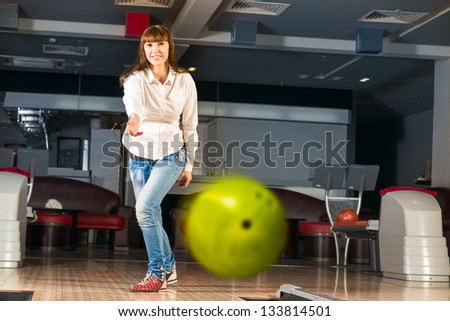 pleasant young woman throws a bowling ball, looks at the target and smiling