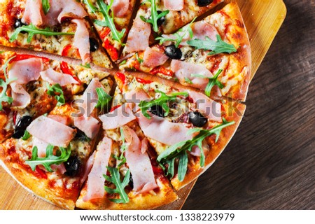 Pizza with Mozzarella cheese, ham, pepper, olive, meat, Tomato sauce, Spices and Fresh arugula. Italian pizza on wooden background