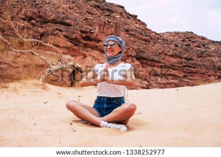 Wilderness nature of rocks, sand and branches around the gorgeous girl who is clothed in leather sneakers, denim shorts, white t-shirt, three color kerchief and sunglasses with mirror effect.