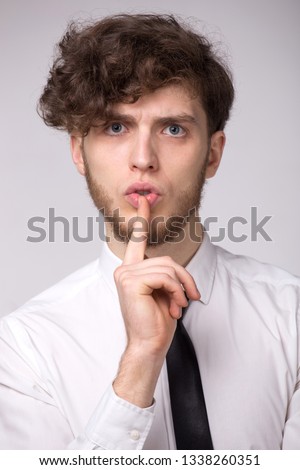 Serious young beard man keeps finger on lips, want to be conspiracy or make silence, on gray background